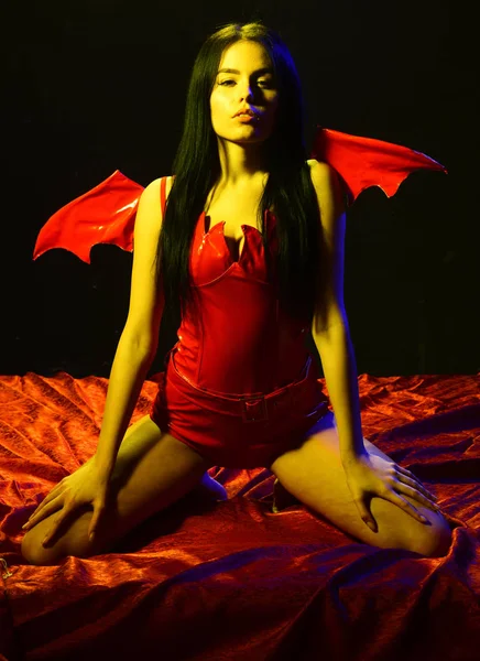 Concepto de diablo sexy. Chica sexy demonio con alas, diablo lleno de deseo. Mujer en la cara apasionada juego de rol. Lady Sexi vestida de demonio, diablo, fondo negro. Demonio sexy chica sentarse en seda hojas — Foto de Stock