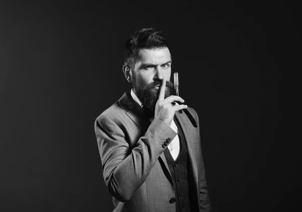 Businessman with secret face on dark red background. Macho in formal suit shows silence sign. Man with long beard holds blade for razor. Barbershop advertising — Stock Photo, Image