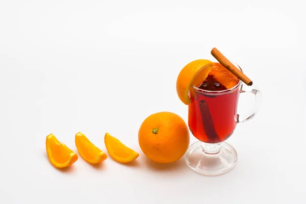 Beber o beber con naranja y canela. Concepto de cóctel y bar. Copa con vino caliente o sidra caliente cerca de fruta naranja y rebanadas sobre fondo blanco. Vino caliente cerca de rebanadas de naranja —  Fotos de Stock