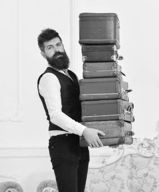 Butler ve hizmet kavramı. Sakal ve bıyık Klasik takım elbise sunar Bagaj, lüks beyaz iç arka plan giyen adam. Maço, zarif porter ağır yığını vintage bavul taşır.