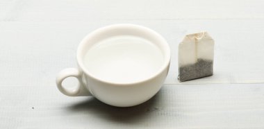 Kupa su ve çay poşeti beyaz zemin üzerine kaynar ile dolu. Çay zaman kavramı. Fincan ya da beyaz Porselen Kupa şeffaf sıcak su ve çay kuru çanta ile. Süreç içinde seramik kupa demleme çay