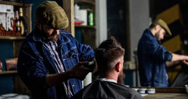 Reflexion of barber with clipper trimming hair of client. Hipster client getting haircut. Hipster lifestyle concept. Barber with hair clipper works on haircut of bearded guy, barbershop background