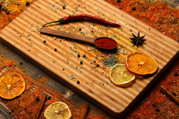 Concetto di arte culinaria. Spezie sparse per il tagliere. Cucchiaio con spezie su struttura in legno. Cucchiaio pieno di cannella, pepe rosso macinato e curcuma in polvere adagiato sul tagliere — Foto Stock