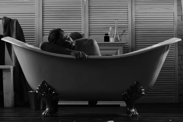 Guy in badkamer met toiletartikelen en stoel op achtergrond. Seksualiteit en ontspanning concept: macho liggend naakt in Bad — Stockfoto