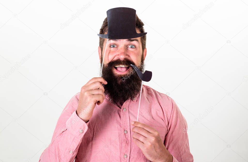 Hipster with beard and mustache on happy face posing with photo booth props. Guy smokes tobacco pipe. Aristocracy concept. Man holding paper party props tobacco pipe and top hat, white background