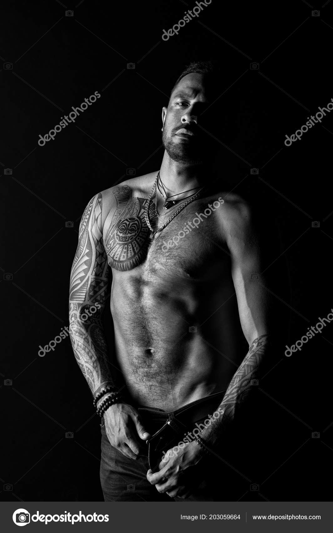 Fashion model buckle leather belt in jeans. Man with tattoo design on skin. Bearded man shirtless Fashion model buckle leather belt in jeans. Man with tattoo design on skin. Bearded man shirtless