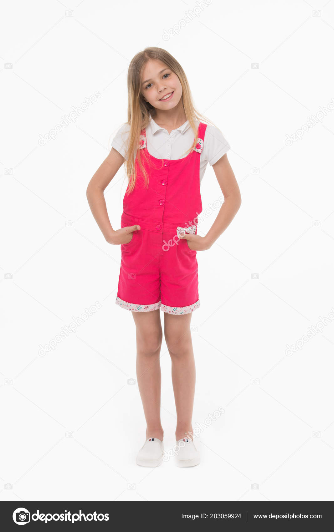Chica con mono rosa caliente, blusa blanca y zapatos. Niño alegre en traje  de verano, concepto de vacaciones. Niño cogido de la mano en los bolsillos.  Chica encantadora con el pelo largo