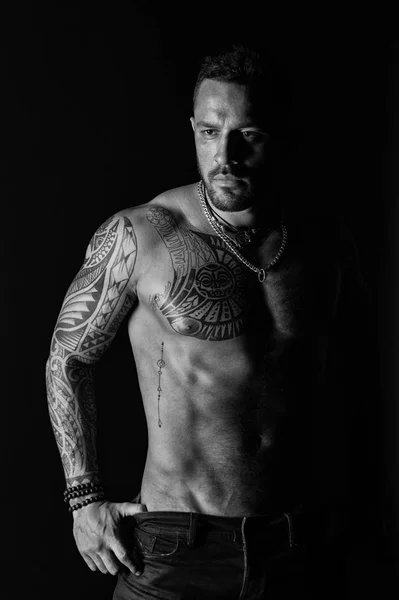 Tattoo model with sexy belly. Man with tattooed arm and chest. Bearded man with strong torso. Sportsman or athlete in fashion jeans. Bodycare with fitness and sport, black and white — Stock Photo, Image