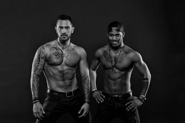 Мужчины с мускулистыми туловищами изолированы на черном фоне. Культуристы с татуировками позируют вместе, спортивная концепция. Мужские модели с сексуальными телами. Улыбающийся африканский парень в бейсболке — стоковое фото
