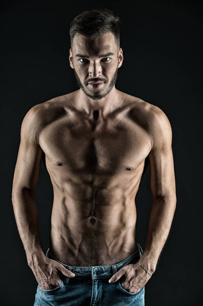 Attractive body. Athlete with muscular body on confident face. Man muscular torso tense muscles veins put hands in pockets denim pants. Macho muscular chest looks attractive black background