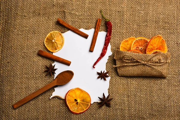 Tarçın, kurutulmuş portakal ve biber, anasonu boş kağıt, tarifi, kopya alanı çevresinde. Çul arka plan üzerinde kağıt parçası. Baharat kaşıkla beyaz kağıt yatıyordu. Mutfak tarifi kavramı