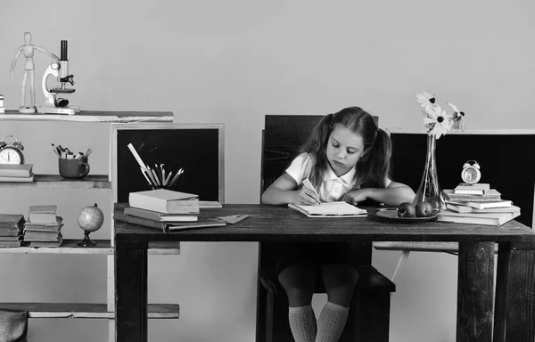 Kız renkli ileti örneğiyle raflar yakınındaki masasında oturuyor — Stok fotoğraf
