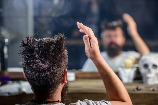 Человек с бородой и усами сидит в парикмахерском кресле перед зеркальным фоном. Рефлексия бородатого клиента парикмахерской. Концепция парикмахерской. Хипстер с мокрыми волосами ждет стрижку, вид сзади — стоковое фото
