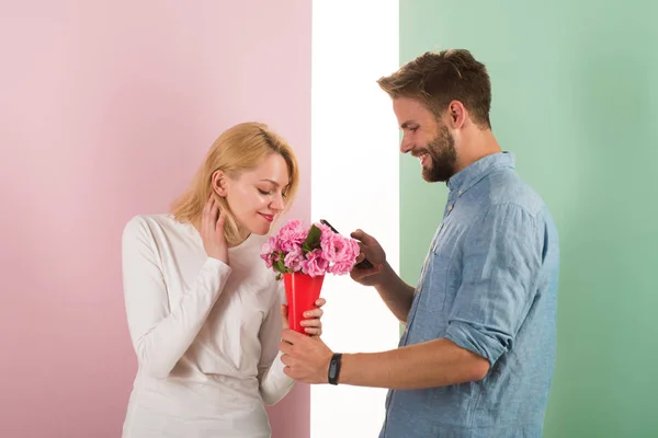 Mannen stilig fina ger blommor till sin flickvän. Online-shop koncept. Man använda telefon att köpa årsdagen gåva online. Kille med telefon och blombukett, pastell rosa och grön bakgrund — Stockfoto