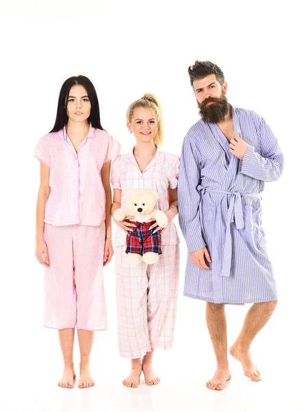 Flickor med skäggiga macho i pyjamas och morgonrock i morgon, isolerade vit bakgrund. Mannen med skägg, Söt blond och brunett flickor med leksak Björn bara vakna upp i morgon. Sömnig morgonen koncept — Stockfoto