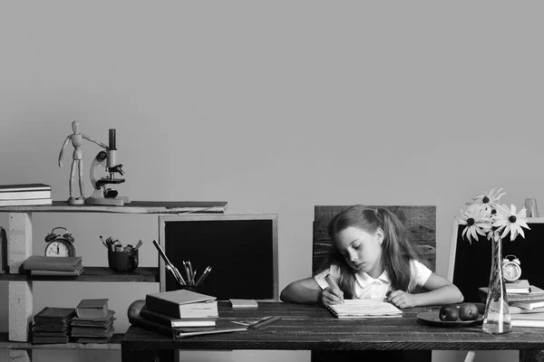 Menina senta-se na mesa com livros, flores, frutas e quadro-negro — Fotografia de Stock