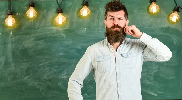 Hombre con barba y bigote en la cara reflexiva de pie delante de pizarra. Hipster barbudo en camisa, pizarra sobre fondo. Un tipo que piensa con expresión reflexiva. Concepto de tarea intelectual — Foto de Stock