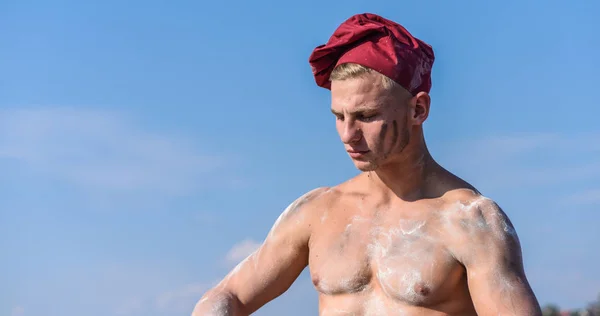 Chef en chapeau de marsala sur le ciel du visage strict sur le fond. Concept de chef sexy. Homme avec l'aspect attrayant fonctionne comme cuisinier ou boulanger, espace de copie. Homme avec torse musculaire recouvert de farine semble attrayant — Photo