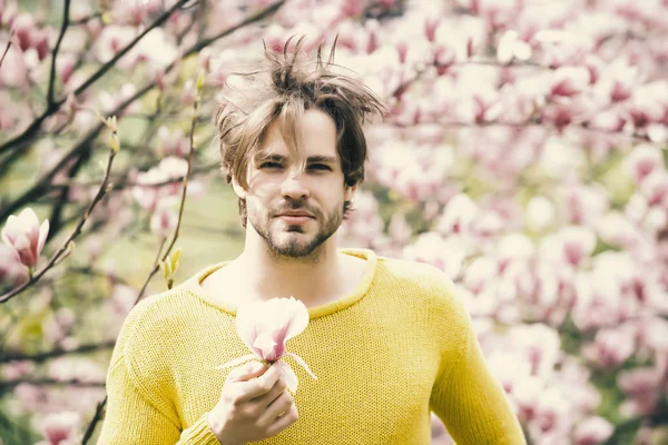 Sakallı, sarı süveterli, çiçekli bir maço.