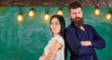 Sakal ve gözlük stand sırt sırta, kara tahta arka plan öğretmen olan adam. Öğretmen ve öğretmen rahat görünüyor. Okul personeli kavramı. Bayan ve birlikte okulda çalışan hipster
