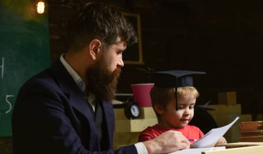 İlköğretim kavramı. Öğretmen ve öğrenci kolej, kara tahta arka plan içinde. Baba oğul öğretir temel bilgi, tartışmak, açıklamak. Çocuk çalışmaları dikkatle dinlerken öğretmenle