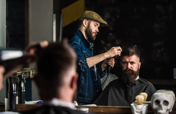 Hipster bearded client getting hairstyle. Barber with hairdryer works on hairstyle for bearded man, barbershop background. Styling concept. Barber with hairdryer drying and styling hair of client — Stock Photo, Image