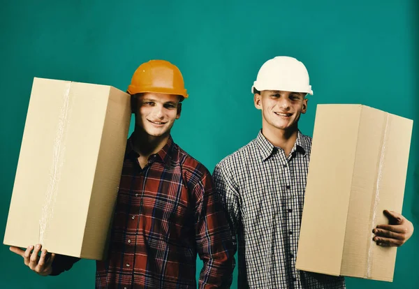 Gémeos com capacetes seguram caixas. Conceito de entrega e movimentação — Fotografia de Stock