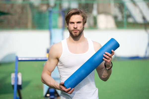 Practicing yoga. Sportsman carries yoga mat for outdoor practicing. Outdoor yoga concept. Man athlete confident face carries mat, going to stretching. Athlete always stretching after workout