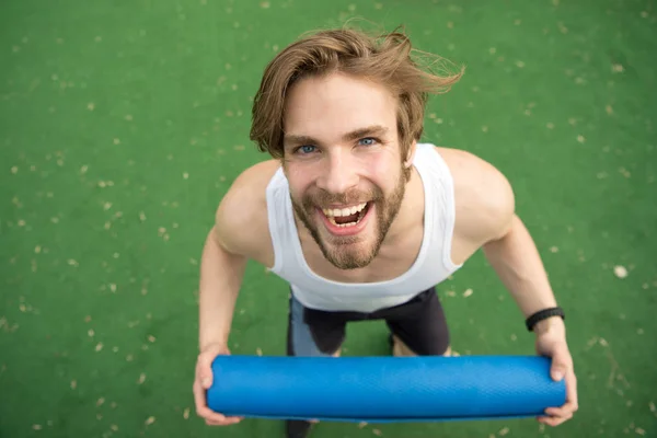 Sträcka på kroppen. Sportsman bär yogamatta för utomhus öva. Utomhus yoga koncept. Idrottaren alltid stretching efter träning. Man bär idrottsman glada ansikte matta, går till stretching — Stockfoto