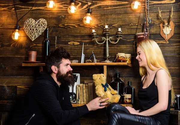 Gülümseyen yüzler üzerinde aşık çift tatilin keyfini çıkarın. Adam Bayan oyuncak ayı için yıldönümü hediye olarak vermek. Yıldönümü kavramı. Çift Romantik akşam gamekeepers evinde, ahşap iç arka plan geçirmek.