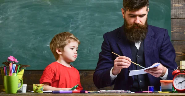 芸術のレッスン コンセプトです。子どもと教師に忙しい顔絵の描画します。ひげ、教師図面を父は、幼い息子の近くでたむろ教室、背景に黒板中 — ストック写真
