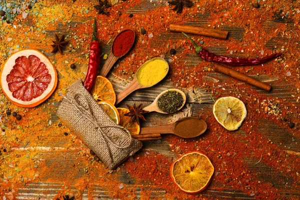 Spices concept. Spoons with spices on wooden texture. Spoons filled with cinnamon, grinded red pepper and curcuma powder and kitchen herbs scattered on table. Spices scattered all over wooden surface