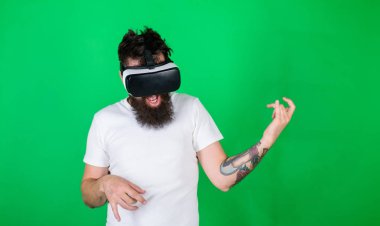 VR gözlüklü adam gitar çalmayı öğreniyor. Hipster gitarist hevesli bir yüz üzerinde modern teknolojiyi eğlence için kullanır. Gözlüklü, yeşil arka planda sakallı bir adam. VR müzisyen konsepti