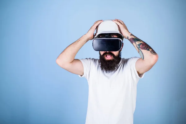 Guy in helmet works as engineer in virtual reality. 3D design concept. Architect or engineer with virtual reality glasses. Man with beard in VR glasses shocked and disappointed, light blue background — Stock Photo, Image