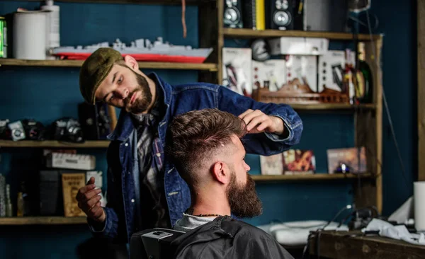 Hipster istemci taze saç kesimi veya saç modeli ile. Styling saç balmumu ile sakallı istemcisinin eller tarafından berber. Berber kavramı. Adam sakal ve bıyık salonların sandalye, arka plan raflarda