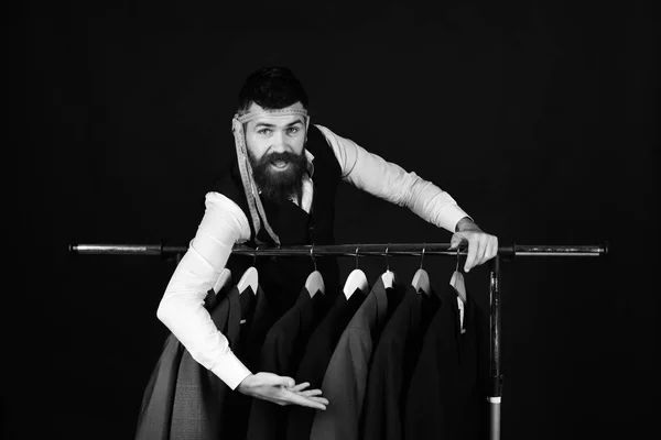 Designer leans on clothes hangers. Man with beard in vest