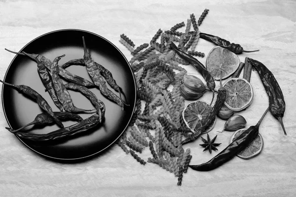 Kırmızı biber ve siyah seramik tabak içinde makarna ve malzemeler.