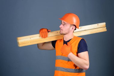 Ahşap malzemeler kavramı. Marangoz, woodworker, ciddi bir yüz taşıdığı ahşap kiriş omuz üzerinde güçlü Oluşturucu. Adam kask, kask ve koruyucu eldiven tutan ahşap kiriş, gri arka plan