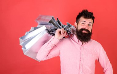 Sakal ve bıyık taşır alışveriş torbaları omuz, kırmızı zemin üzerine olan adam. Hipster serin yüzündeki bağımlısı alışveriş veya Alışverişkoliğin. Satış sezon indirimlerle alışveriş adam. Alışveriş kavramı