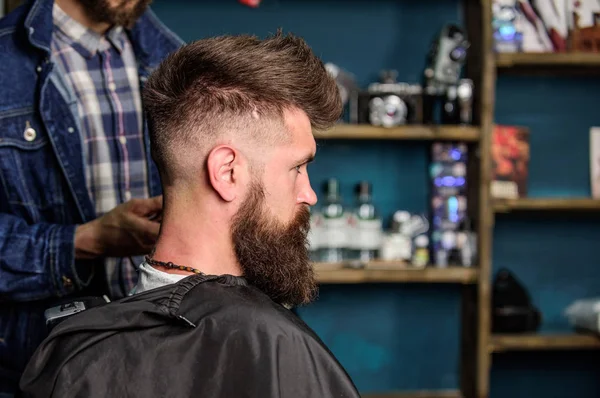 Hairstyle service concept. Hipster bearded client got hairstyle. Barber with clipper works on hairstyle for bearded man, barbershop background. Barber with trimmer or clipper shaved neck of client
