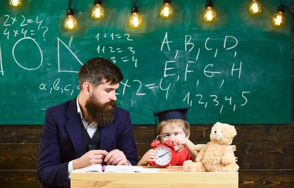 Jovem professor do sexo masculino orienta seu aluno criança para a aprendizagem enquanto sentado em sala de aula com rabiscos em chalkboar — Fotografia de Stock