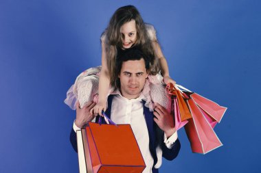 Pembe ve kırmızı paketli kız ve baba. Kendine güvenen ve küstah yüzlü kız ve erkek mavi arka planda alışveriş torbaları tutuyor. Liseli kız babasının boynuna oturur. Alışveriş, hediyeler ve aile kavramı