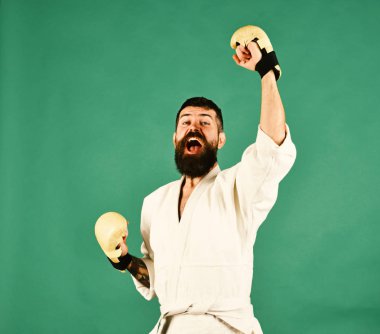 Yeşil zemin üzerine beyaz kimono içinde sakallı adam. Oryantal spor kavram. Savaş usta eller zafer ve bağırır kadar tutar. Düzgün ve altın boks eldiveni yüzüne karate adamla mutlu heyecanlı