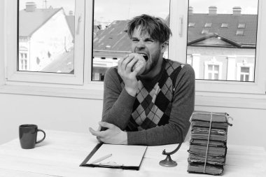 Masasında kitap yığınıyla oturan süveterli bir adam.