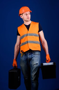 Kask, kask içinde adam araç kutusu ve araç, mavi arka plan ile bavul tutar. Tamirci, tamirci konsantre yüzündeki profesyonel ekipman ile ağır çanta taşır. Profesyonel tamirci kavramı