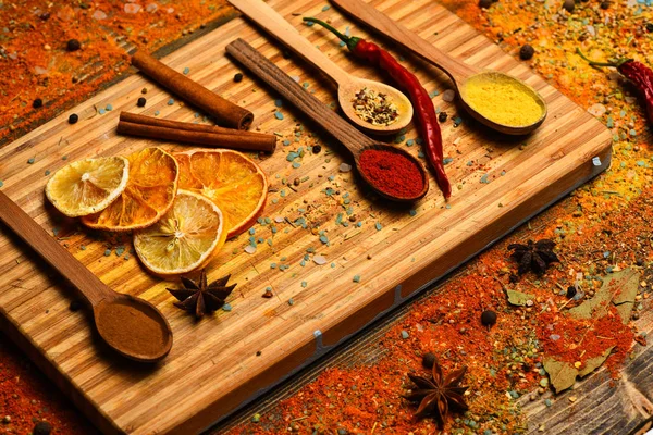 Culinary arts concept. Spoon filled with cinnamon, grinded red pepper and curcuma powder lay on cutting board. Spoon with spices on wooden texture. Spices scattered around cutting board — Stock Photo, Image