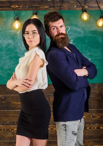 Sakal ve gözlük stand sırt sırta, kara tahta arka plan öğretmen olan adam. Okul personeli kavramı. Bayan ve birlikte okulda çalışan hippi. Öğretmen ve öğretmen rahat görünüyor