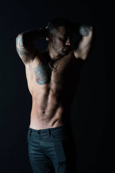 Homem tatuado mostra torso muscular sexy. Esportista com seis maços e abdominais. Fisiculturista com bíceps e tríceps. Modelo de moda com tatuagem em jeans. Cuidado com o corpo com fitness e esporte — Fotografia de Stock