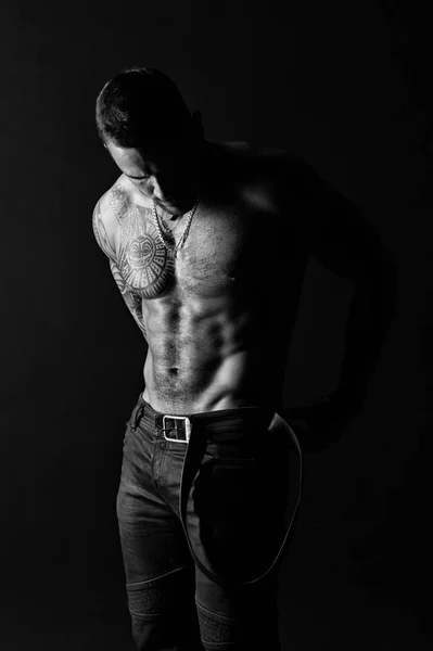 Homem com design de tatuagem na pele. Modelo de moda colocar cinto de couro em jeans. Homem barbudo sem camisa com tronco em forma. Desportista com braço tatuado e peito. Cuidado com o corpo com fitness e esporte, preto e branco — Fotografia de Stock