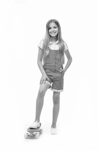 Actividad deportiva y energía. Sonrisa de niña pequeña con tabla de skate aislada en blanco. Patinador infantil sonriendo con longboard. Niño monopatín en mono rosa. Juegos de infancia. Su medio de transporte favorito — Foto de Stock